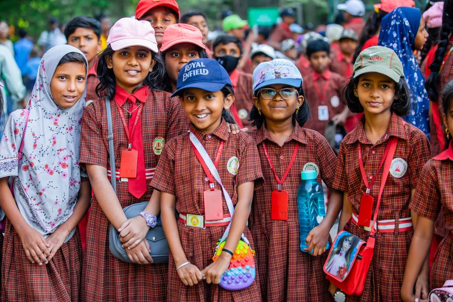 A group of Indian schoolchildren in red-check uniform smiling outdoors