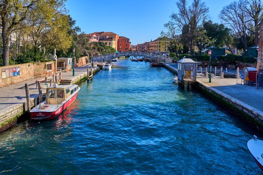 Serene Venetian canal scene with colorful buildings and boats under a clear blue sky.