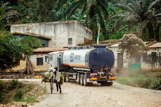 A logistics truck and a cyclist on a rural road lined with houses and palm trees.