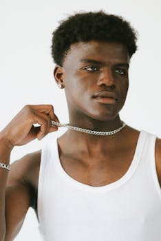 Confident young man wearing a white tank top and chain necklace in a studio portrait.