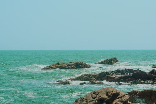 A tranquil seaside view featuring rocks in vibrant turquoise waters under a clear blue sky.