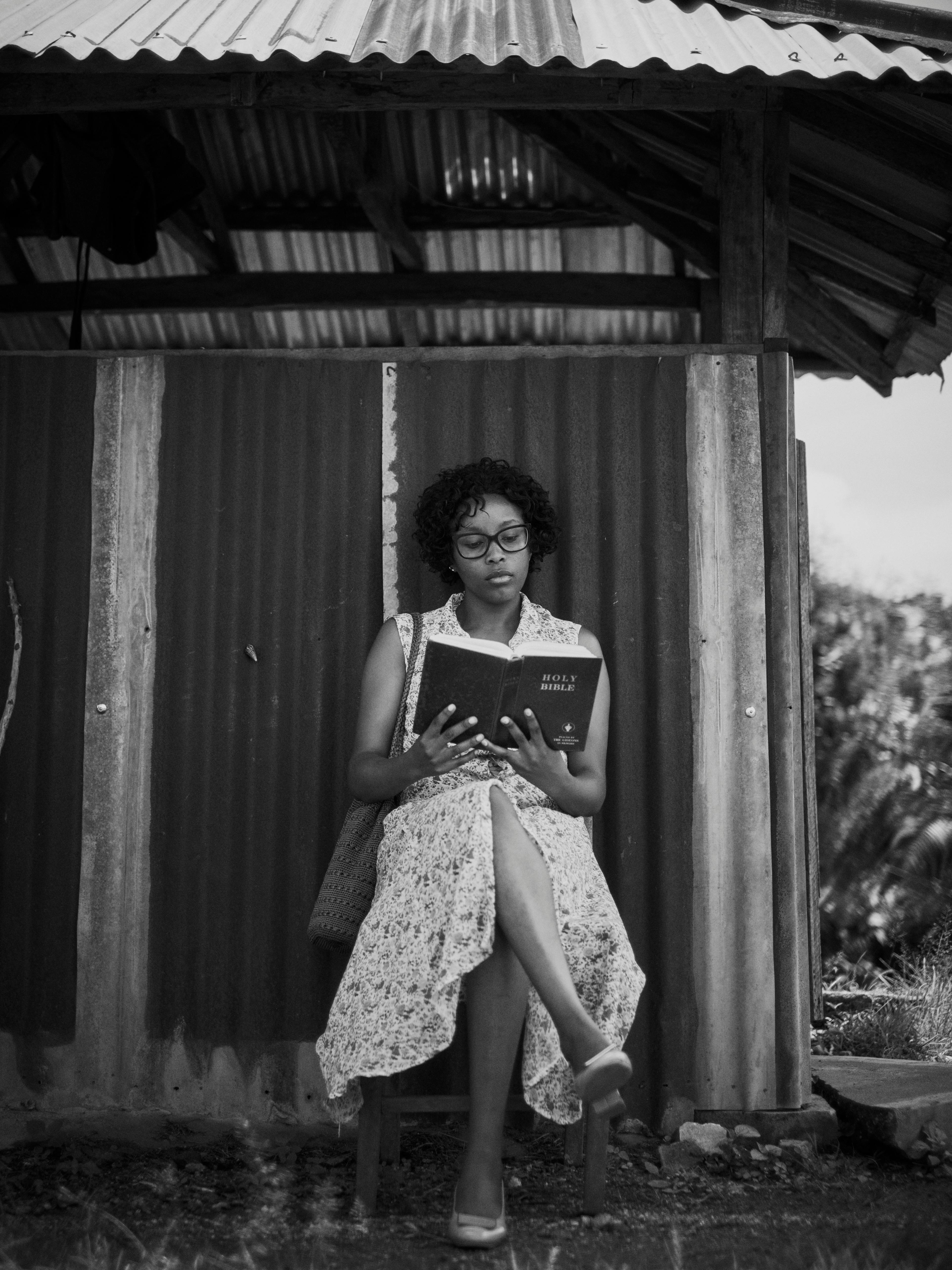 Black and white photo of a woman reading the Bible outdoors, serene and thoughtful.