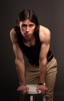 Portrait of a fit young man with long hair leaning on a stool in a studio setting.