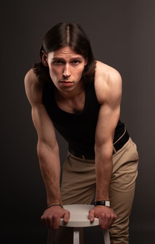 Free Portrait of a fit young man with long hair leaning on a stool in a studio setting. Stock Photo