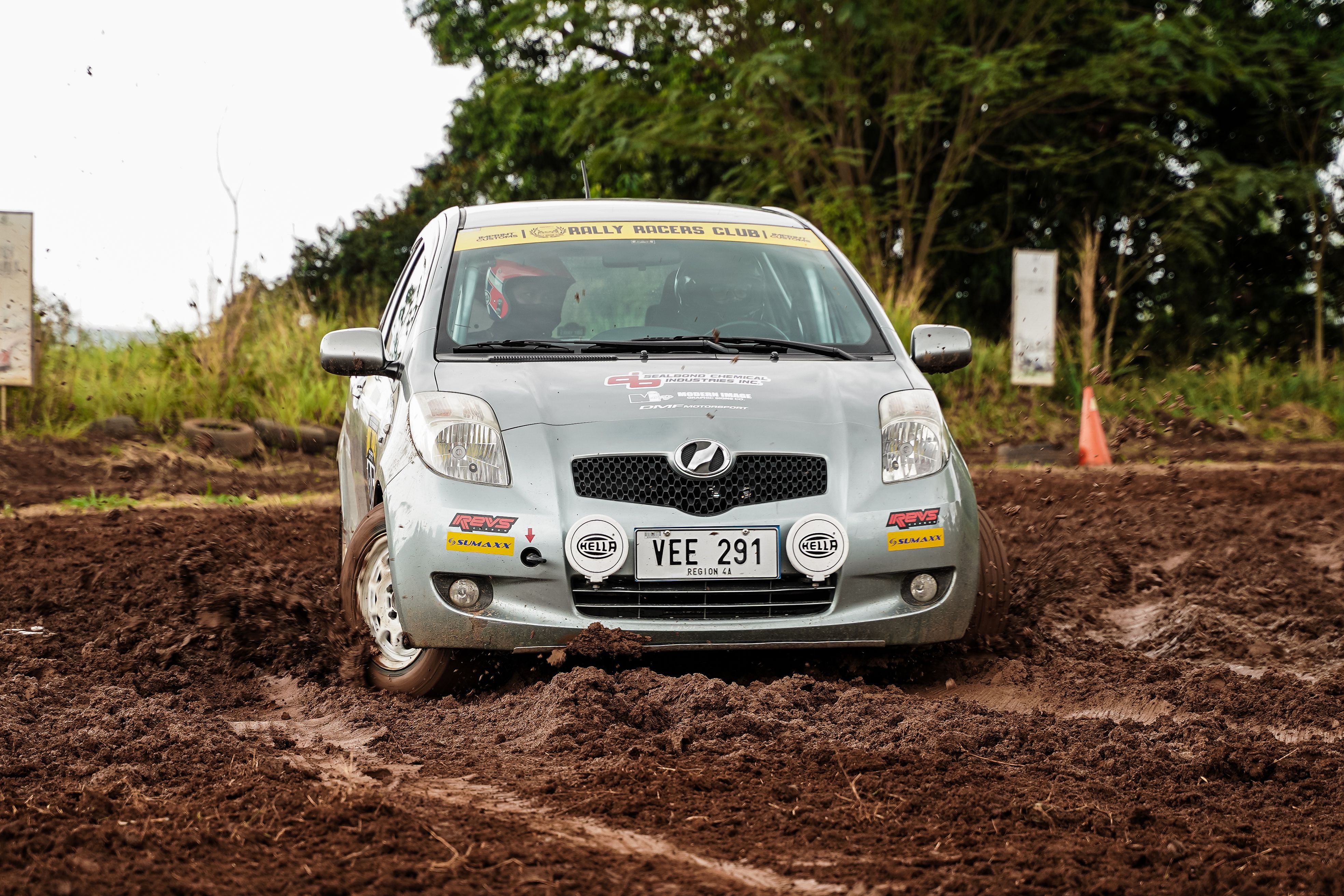 A rally car speeds through muddy terrain, kicking up dirt during an exciting outdoor race.