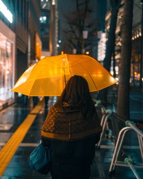 A woman walks under a yellow umbrella on a rainy night in Tokyo, Japan.