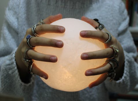 Hands with rings holding a glowing crystal ball, creating a mystical atmosphere.