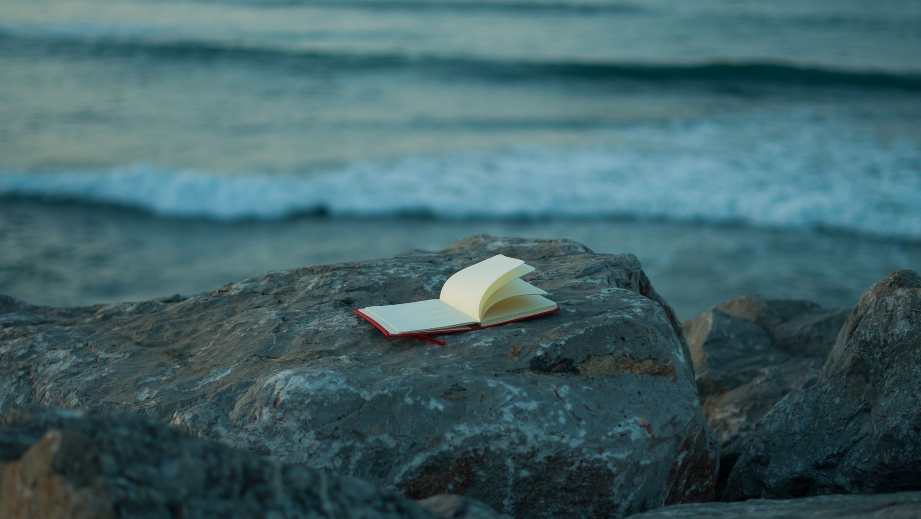 An open notebook on a rocky coastline at dusk, closer to remembrance than reinvention.
