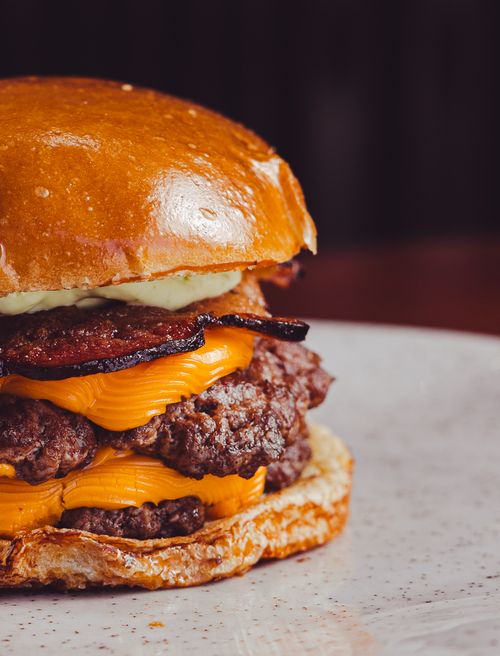 Free Juicy cheeseburger topped with crispy bacon and cheddar cheese on a white plate. Stock Photo
