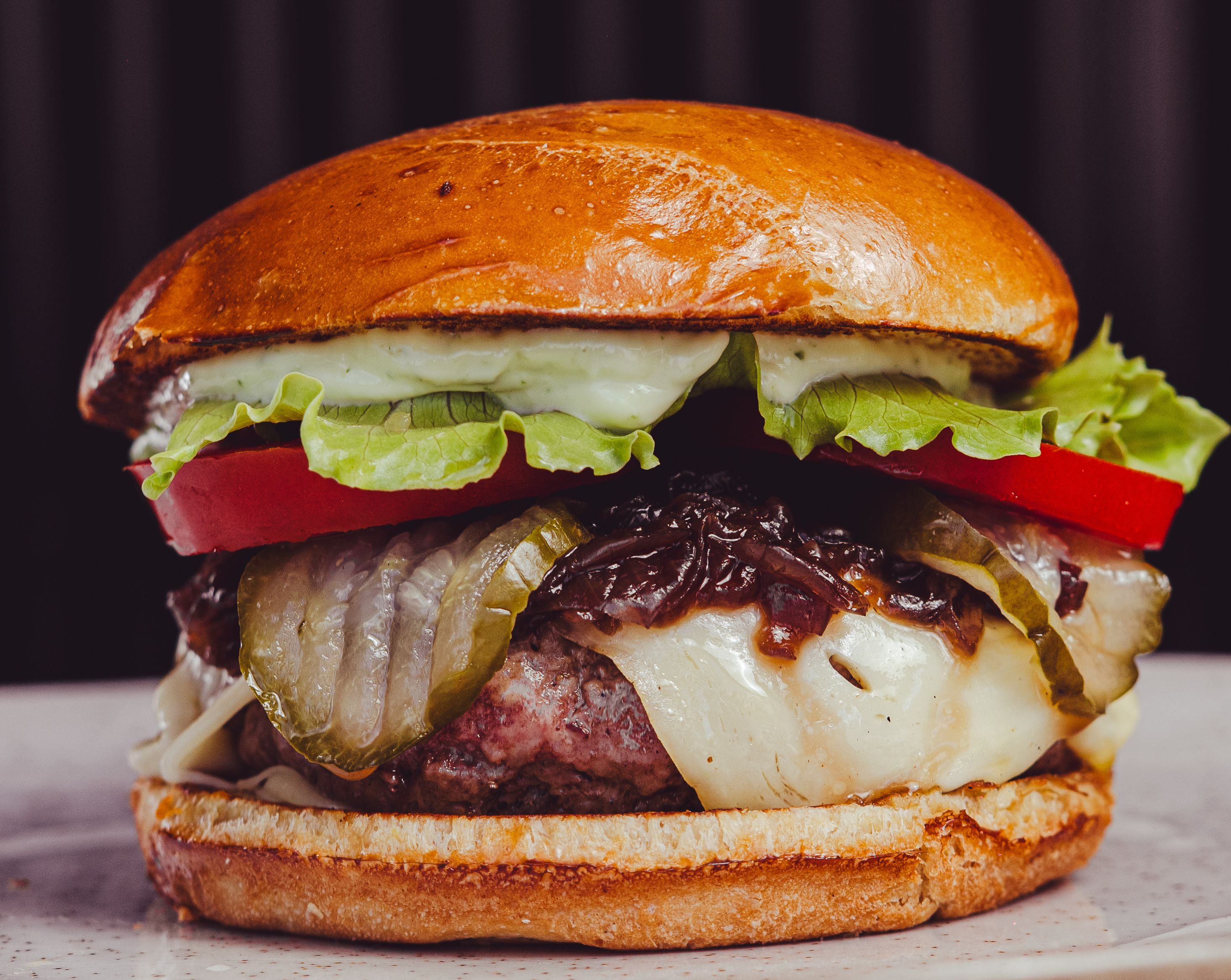 Close-up of a juicy cheeseburger with lettuce, tomato, pickles, and onions on a plate.