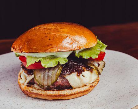 Tasty cheeseburger with lettuce, tomato, pickles, and onions on a white plate.