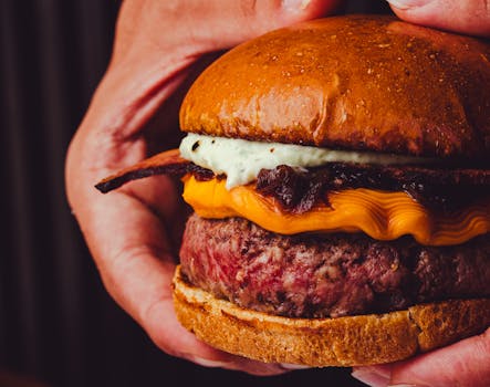 Delicious gourmet cheeseburger with bacon, cheddar, and creamy sauce held between hands.