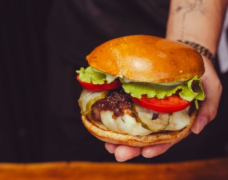 Close-up of a gourmet cheeseburger with fresh lettuce, tomatoes, and melted cheese in a person's hand.
