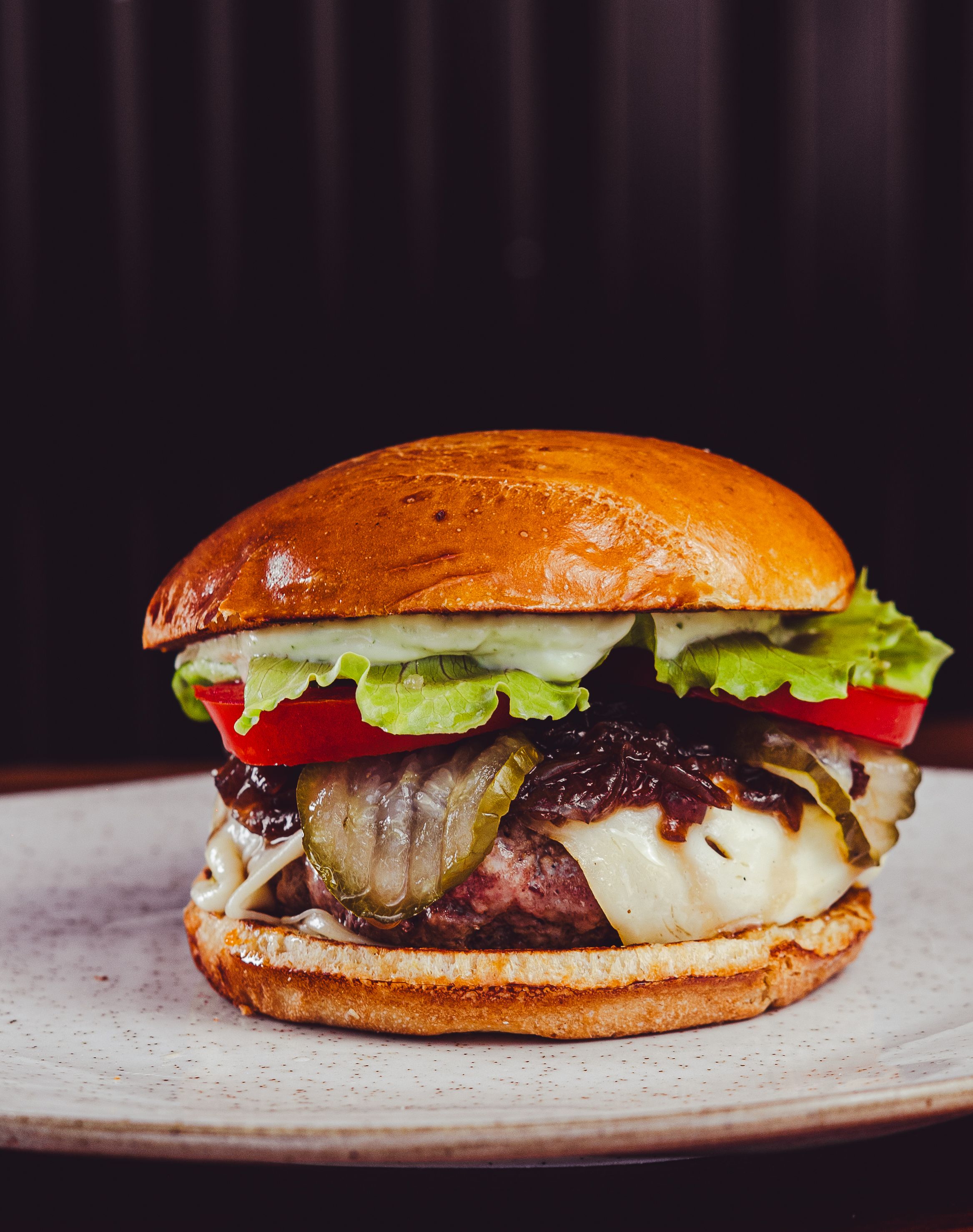 Close-up of a gourmet cheeseburger with fresh toppings on a ceramic plate.