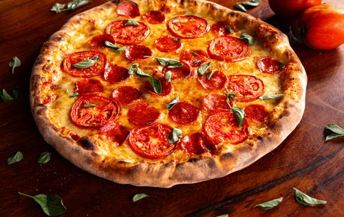 Free Close-up of a fresh pepperoni and tomato pizza with basil leaves on a rustic wooden table. Stock Photo