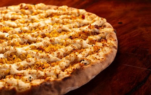 Free Close-up of a perfectly baked sweet corn pizza with creamy cheese spread on a wooden tabletop. Stock Photo