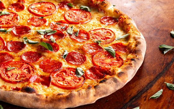 Close view of pizza with pepperoni, fresh tomato slices and basil on dark wood
