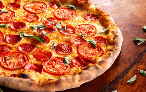 Free Mouthwatering pizza topped with fresh tomatoes, pepperoni, and basil on a rustic table. Stock Photo