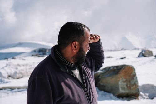 Free A bearded man surveys a snowy mountain landscape under a bright winter sky. Stock Photo