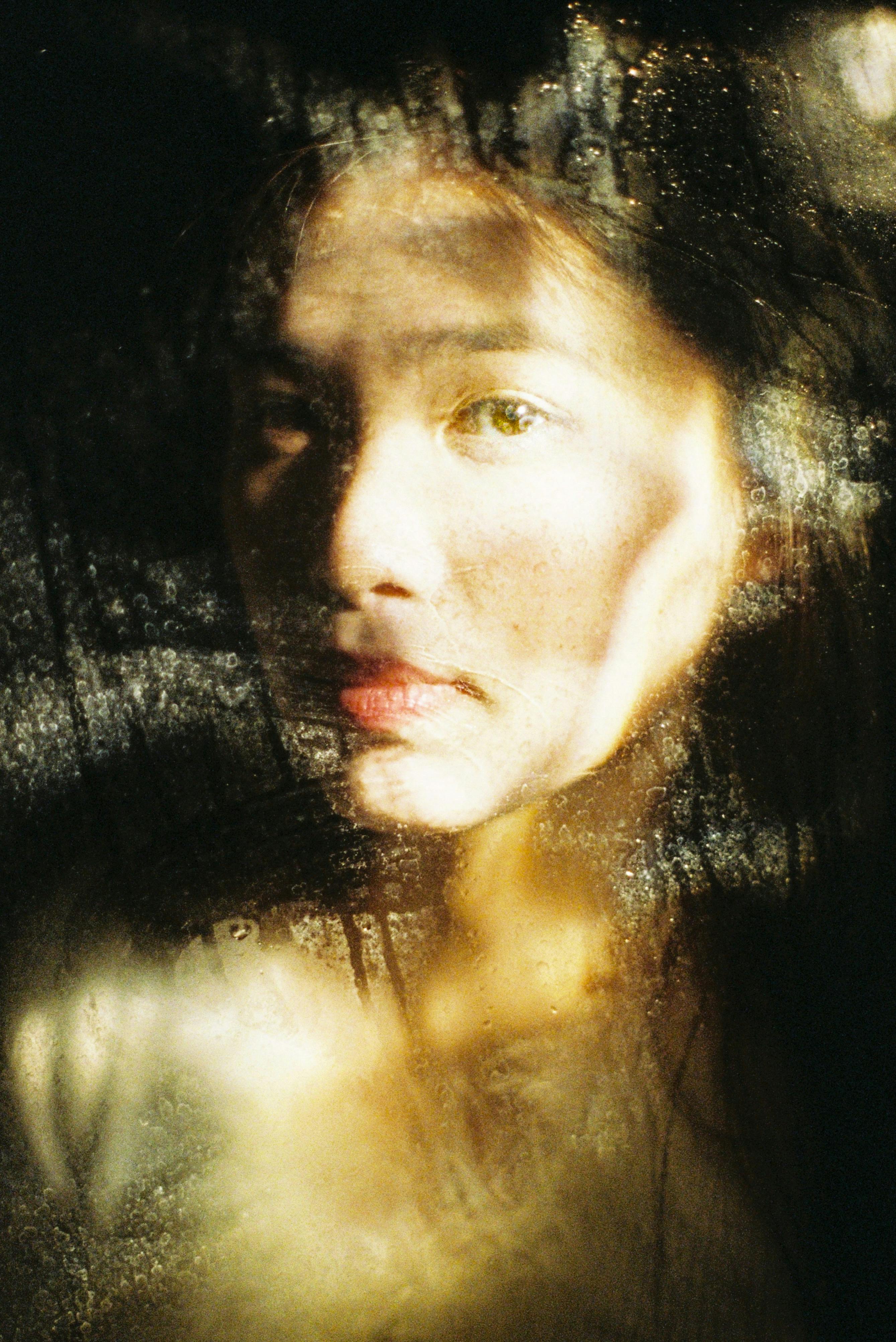 An expressive portrait of a woman with sunlight creating dramatic shadows through glass.