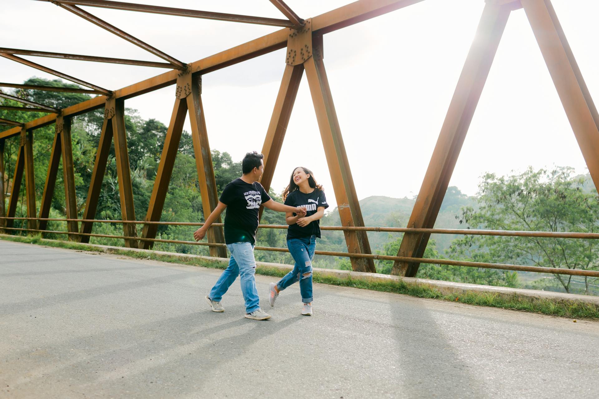 Joyful couple dancing on an iron bridge in Davao City amidst a scenic outdoor setting.