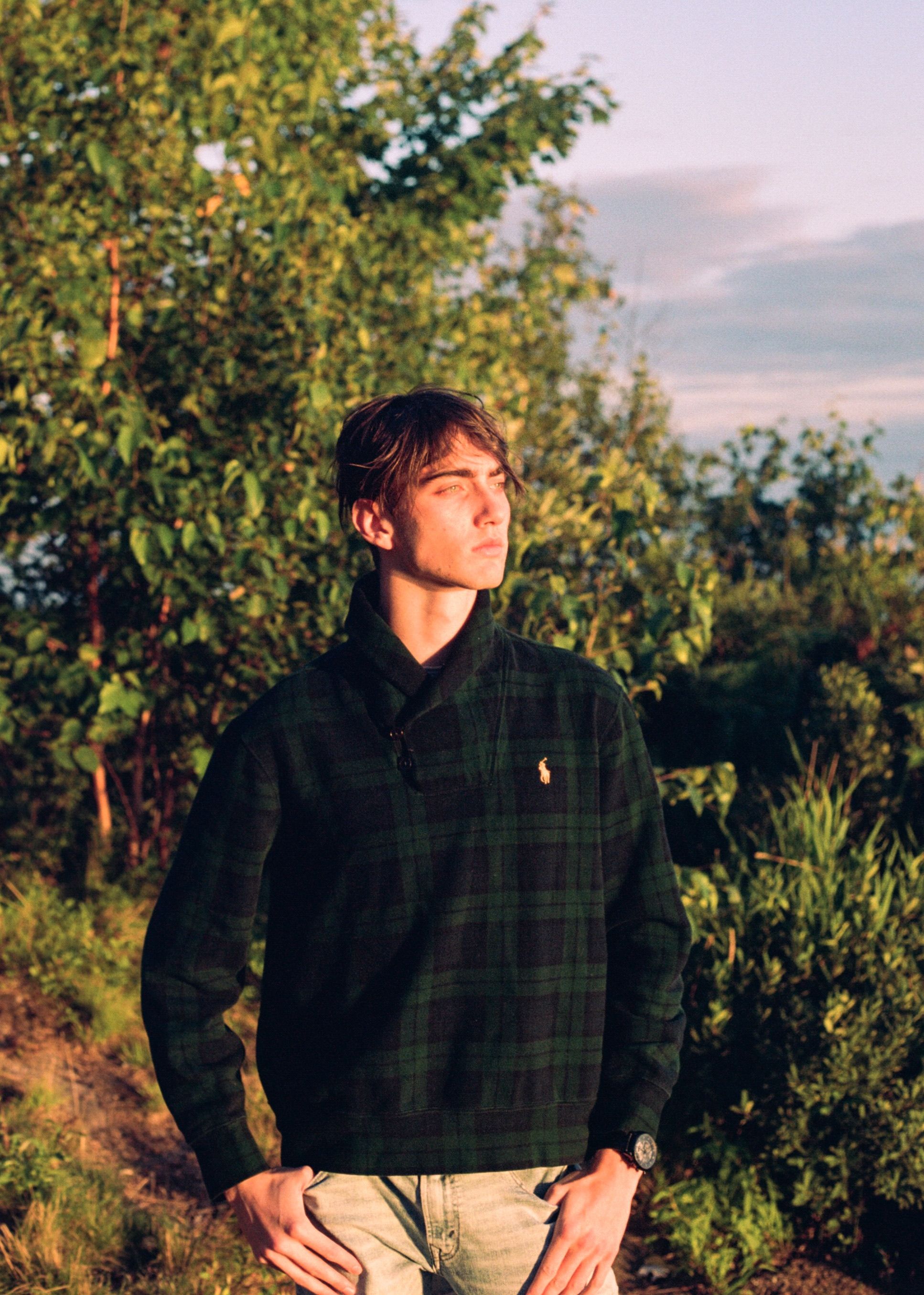 Young man in casual attire posing confidently outdoors during sunset.