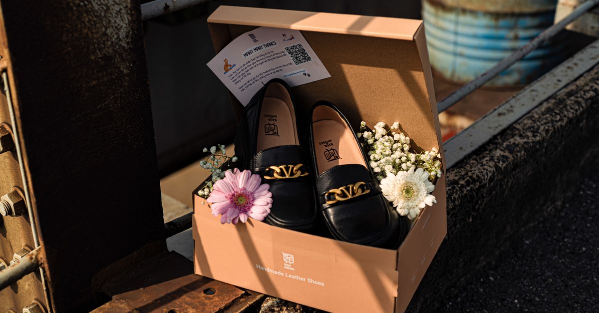 Black leather shoes with gold chain in box, adorned with flowers, in an industrial setting.