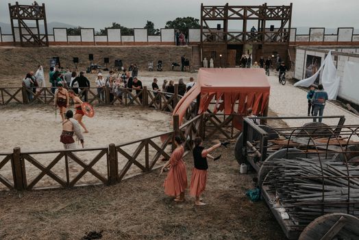 Lively medieval reenactment event featuring gladiators and spectators in outdoor arena.