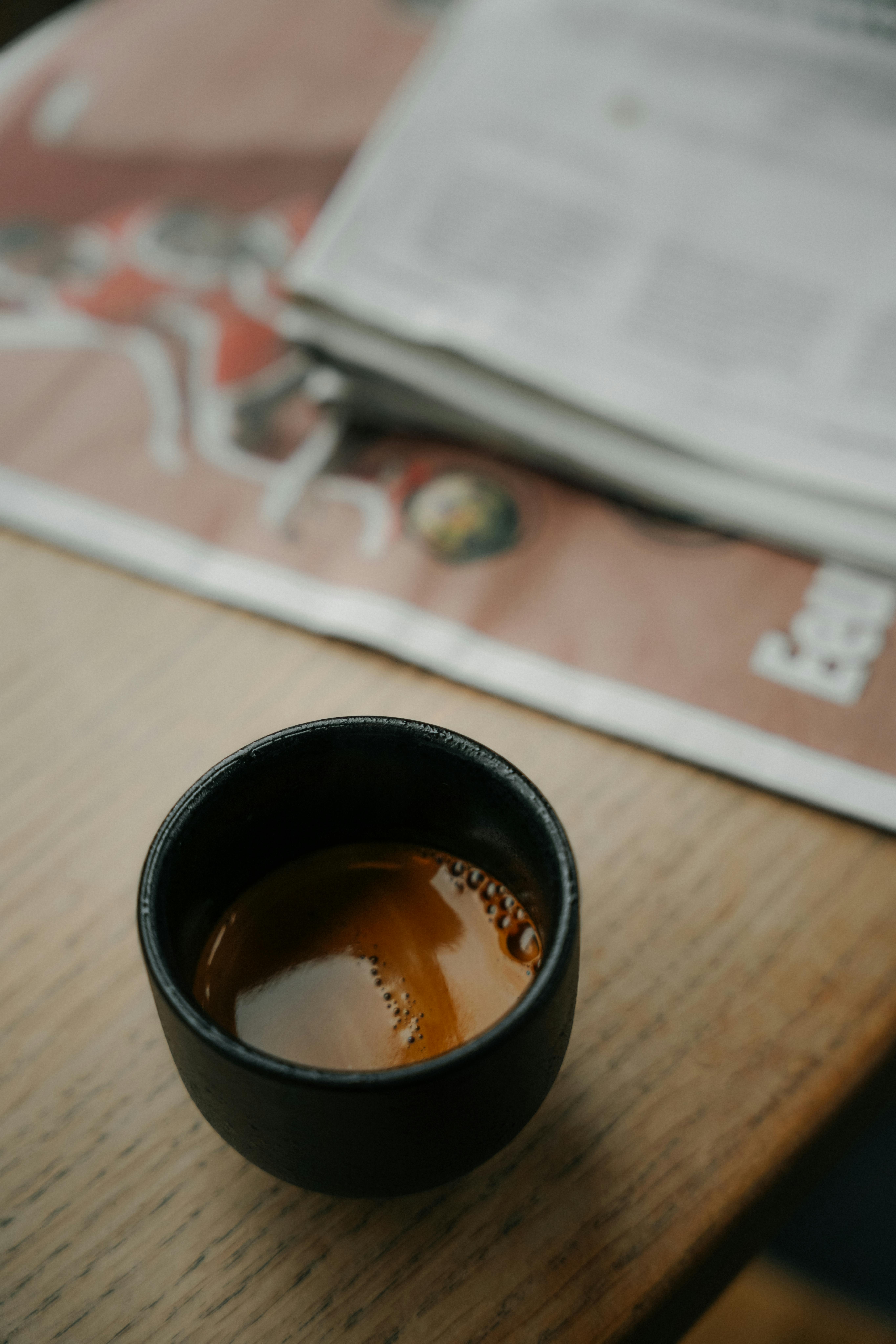 A warm espresso cup on a wooden table with a newspaper in Amsterdam café.