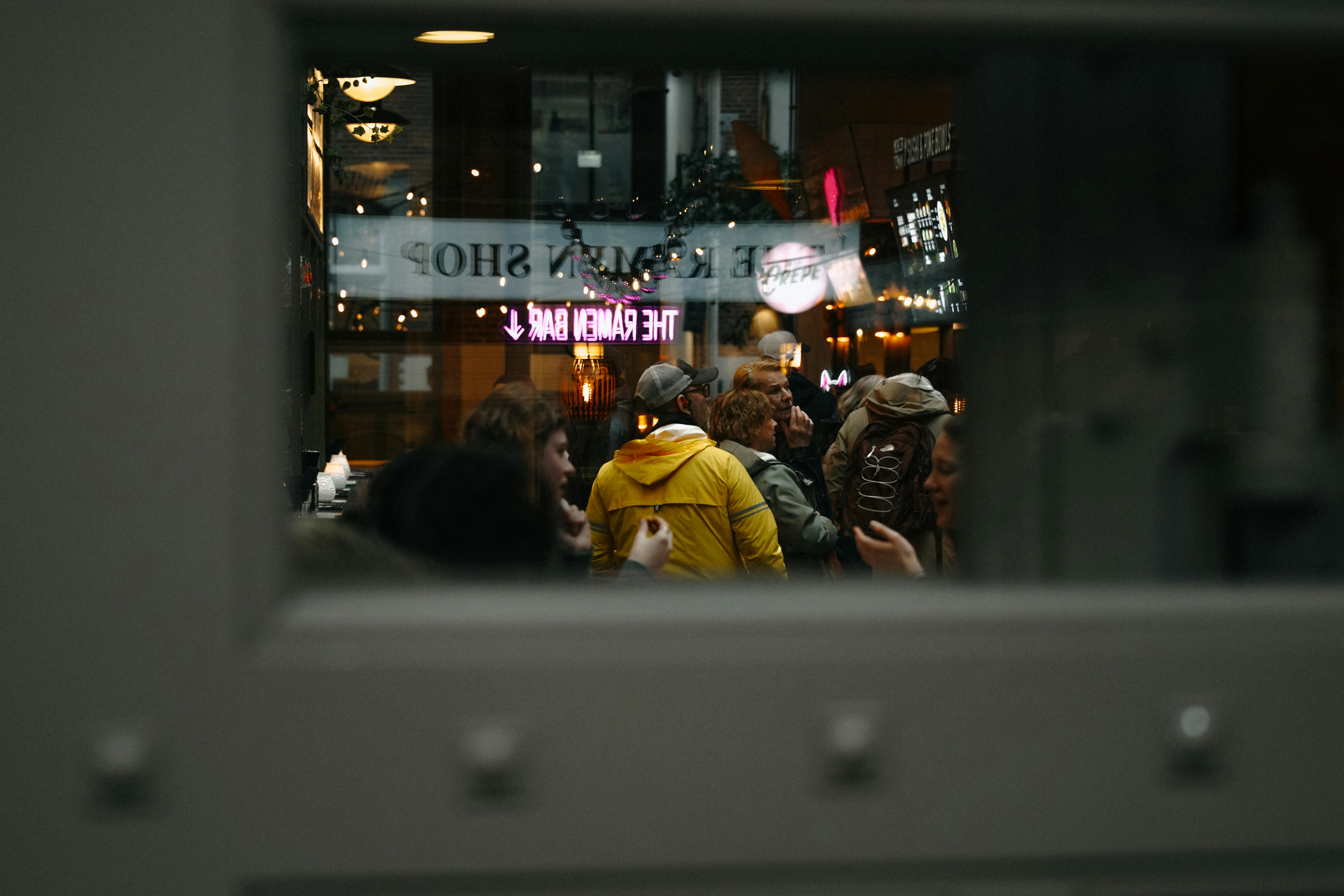 bezplatná Atmosférický pohled oknem kavárny v Amsterdamu ukazuje lidem, kteří si užívají pulzující večer. Základová fotografie