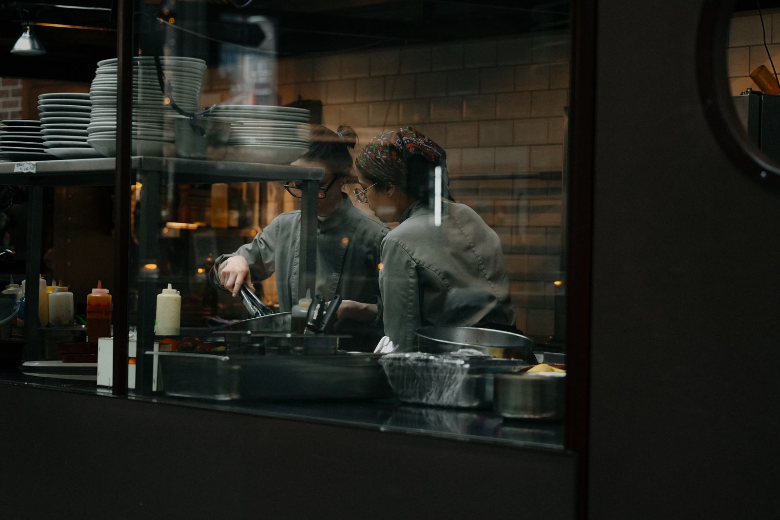 Two chefs working in a busy restaurant kitchen viewed through a window — What's on the menu at Hondumex Sabor Latino in Houston — Hondumex Sabor Latino, Houston
