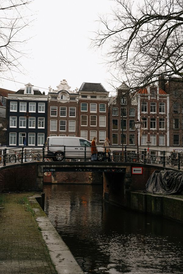 Canal din Amsterdam cu pod și copaci cu frunze aurii de toamnă