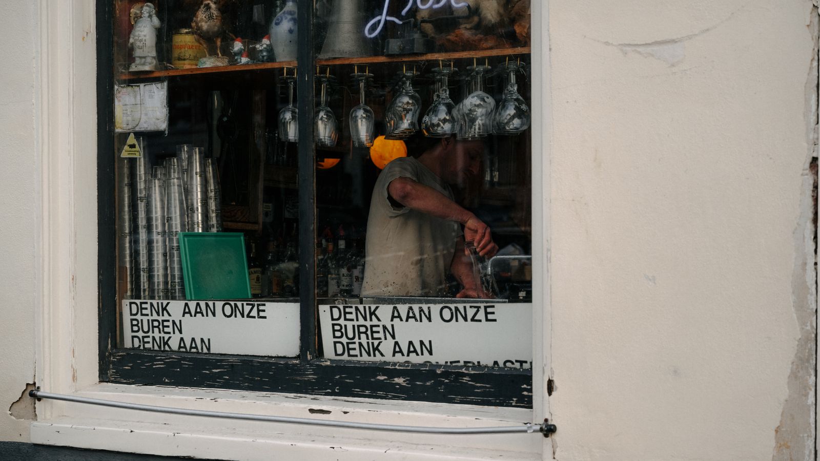 A bar window in Amsterdam showcases glasses and signage, reflecting urban charm.