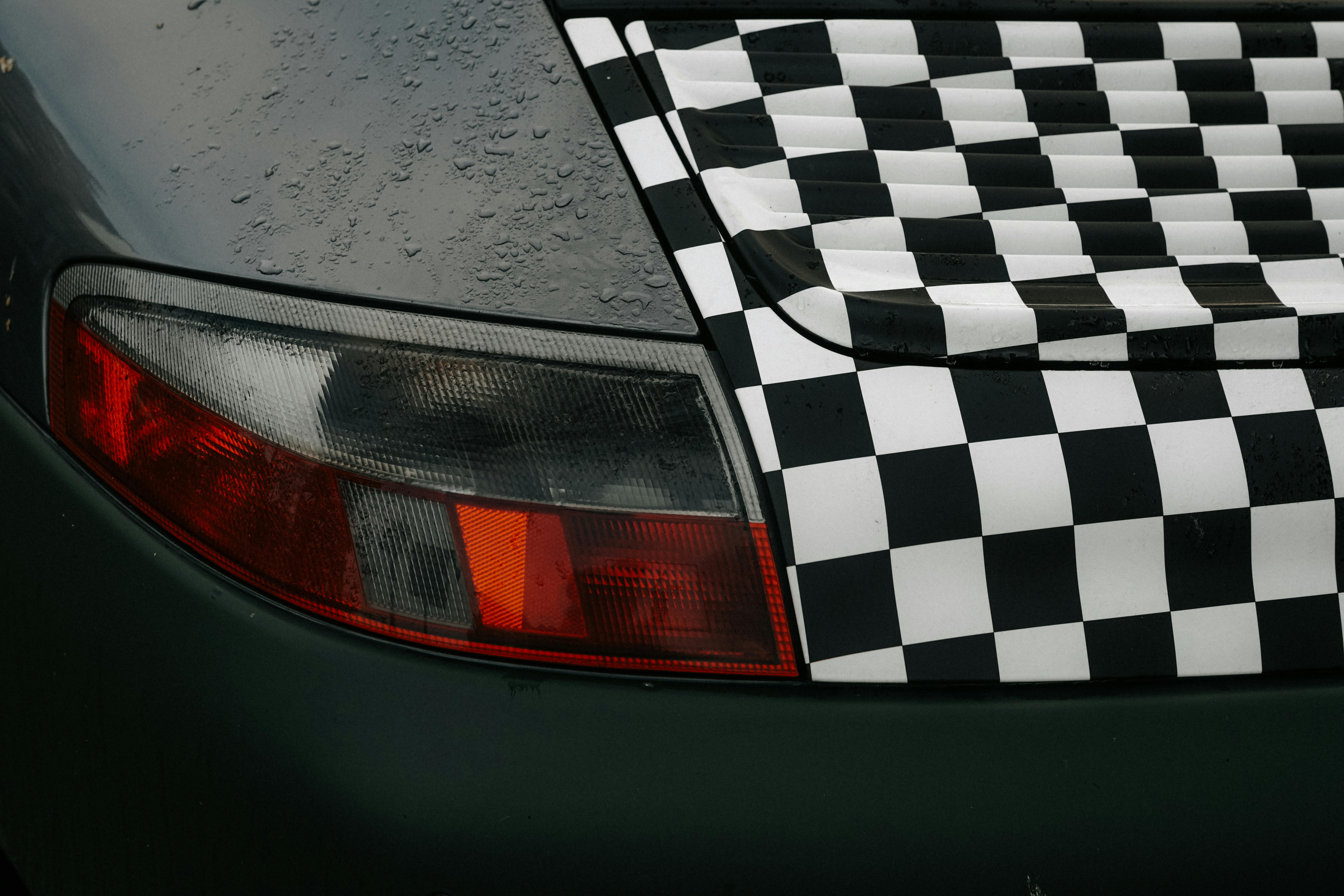 Close-up of a car's tail light with a black and white checkered pattern in rainy conditions in Amsterdam.
