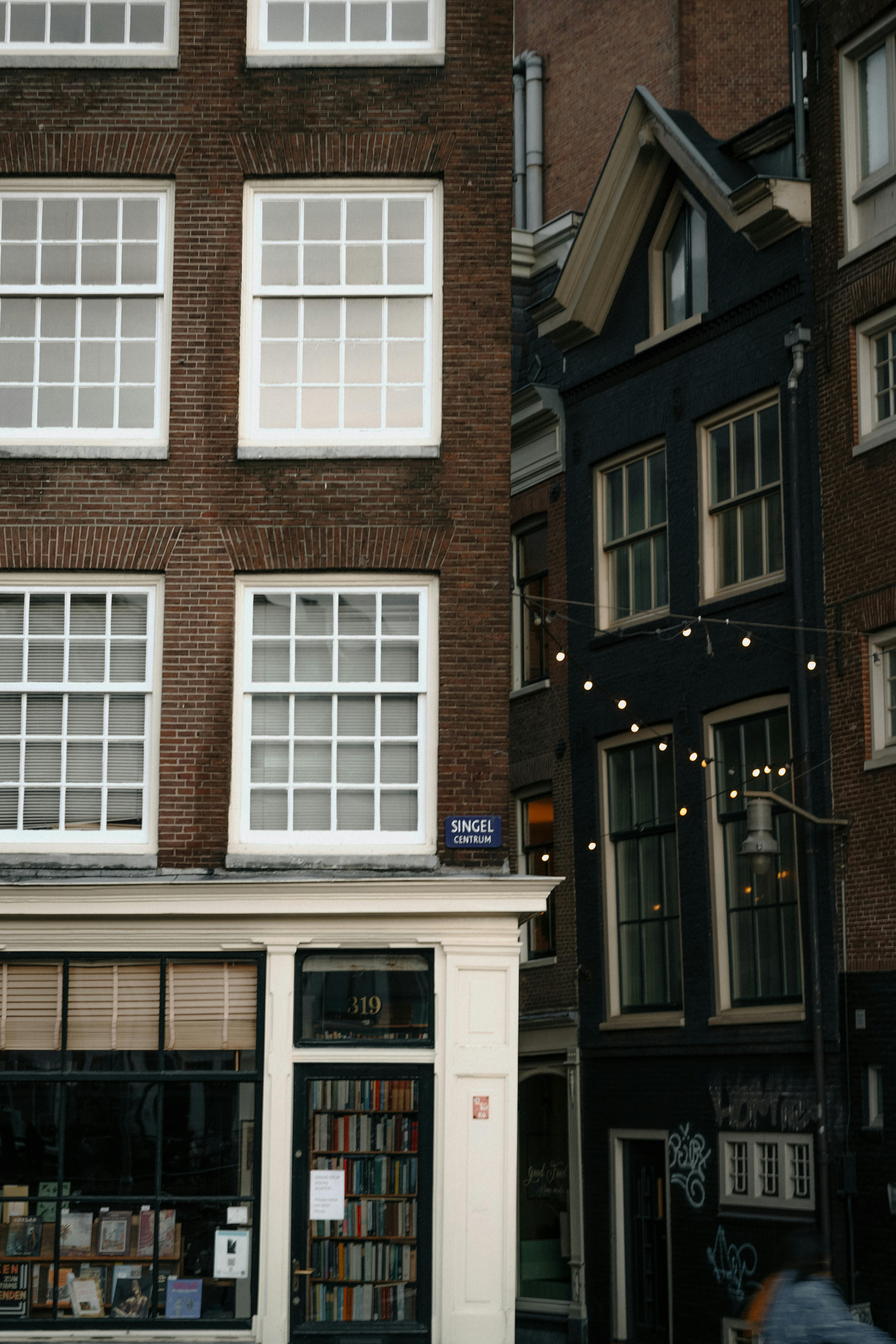 Explore a picturesque Amsterdam street featuring iconic canal houses and a cozy bookshop facade.