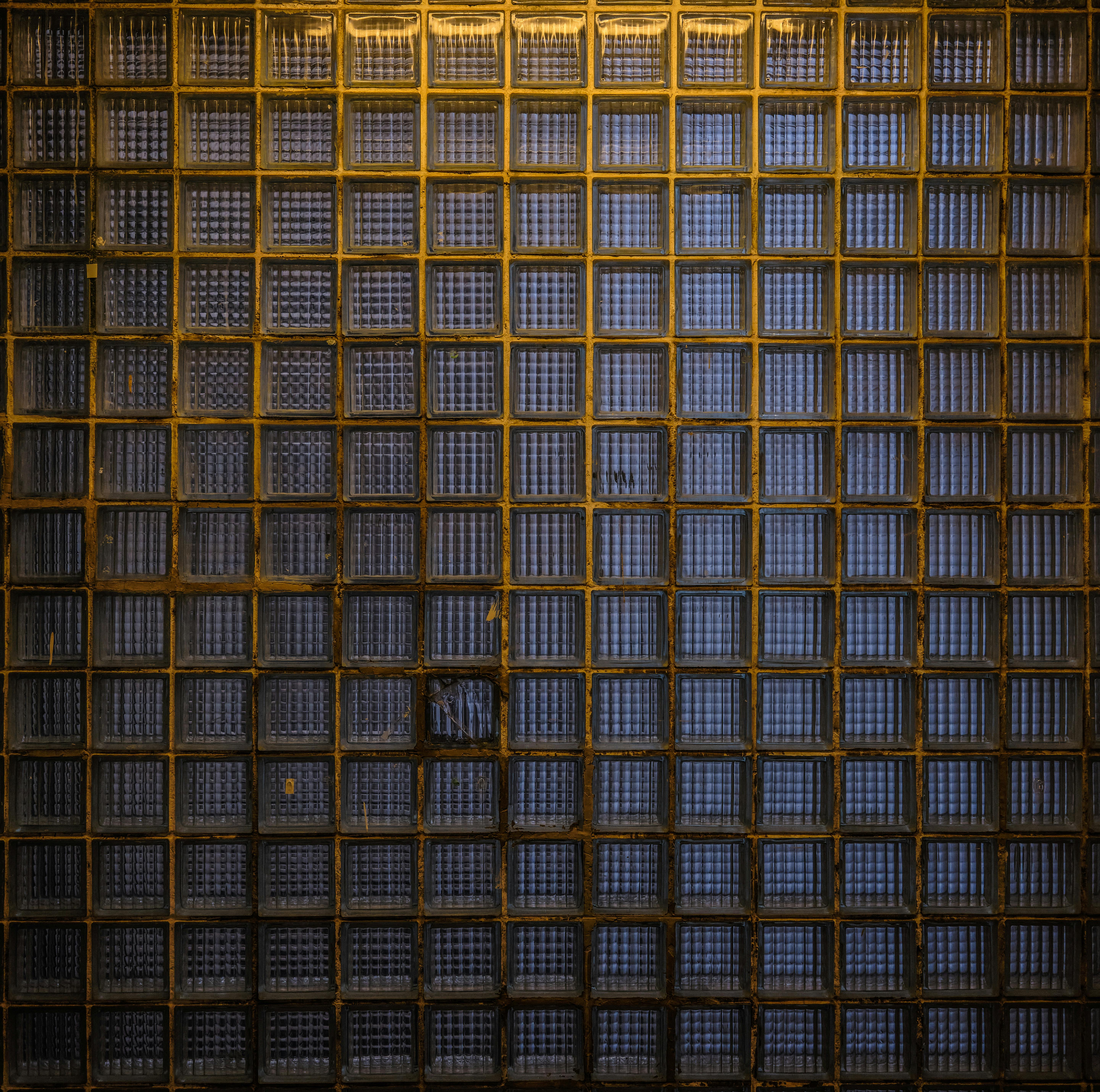 Gratis Detaljeret visning af en tekstureret glasmurstensvæg med et metalgitter, der viser geometriske mønstre og industrielt design. Lagerfoto