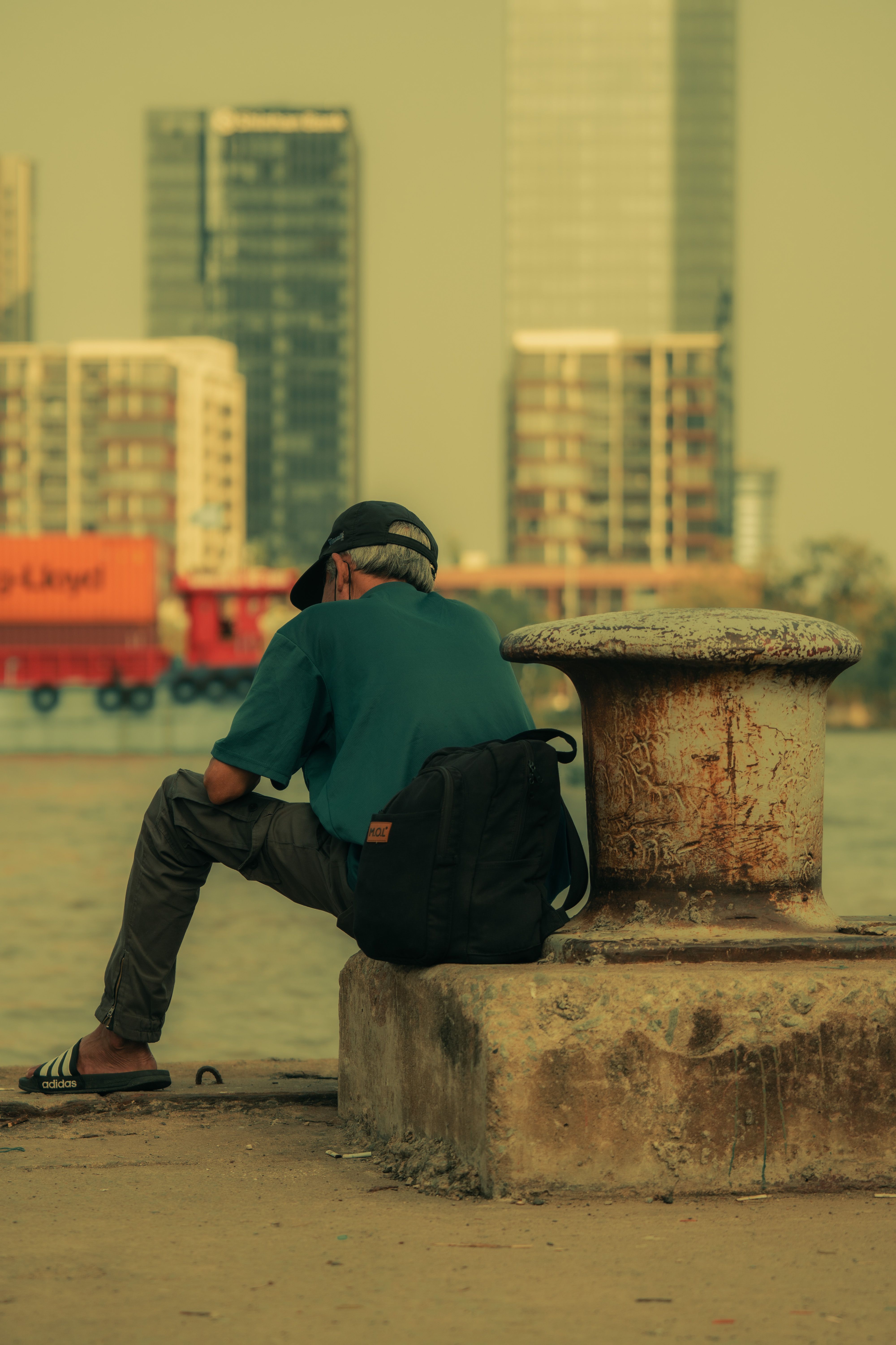 A person sitting alone by an urban waterfront, gazing at the city skyline