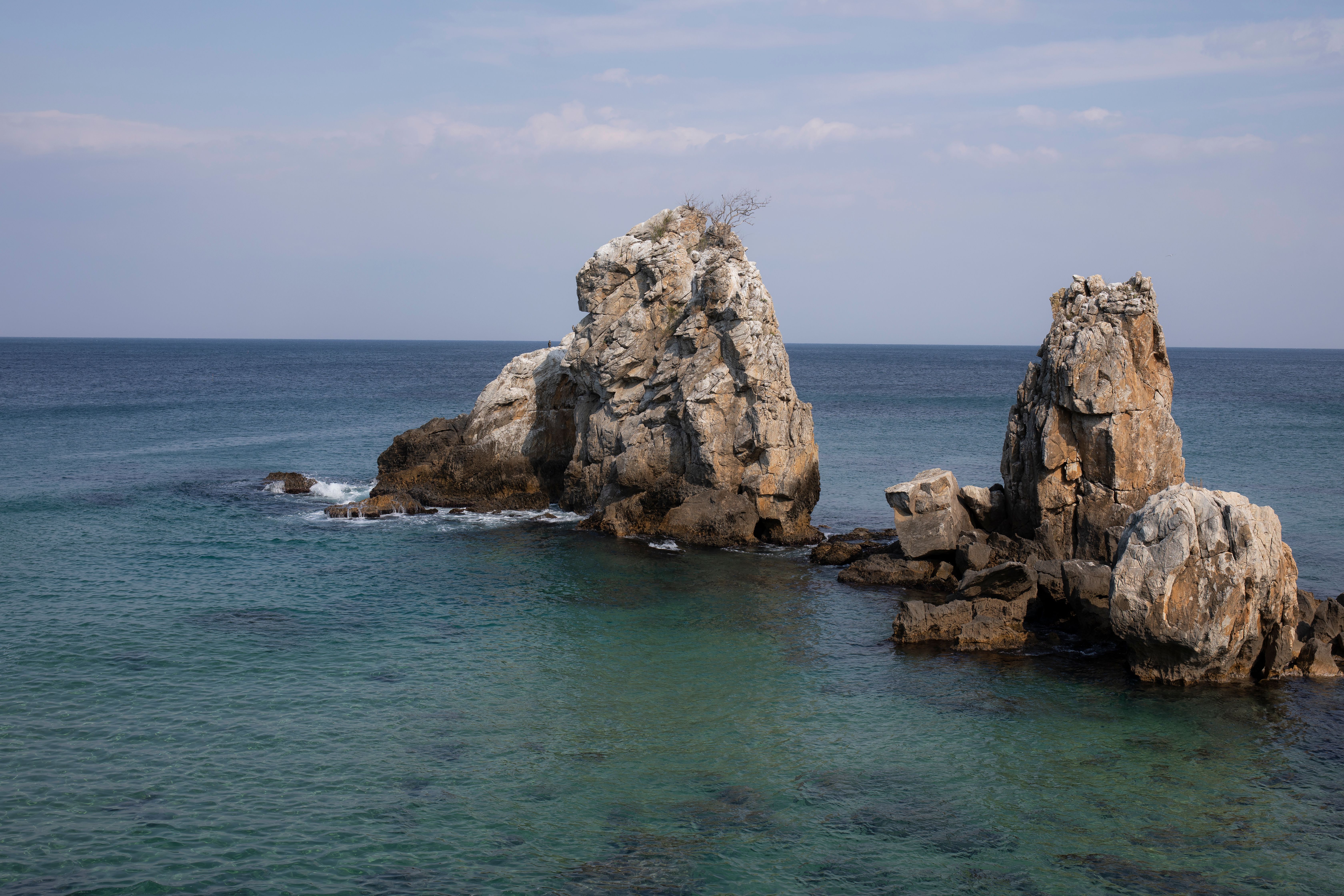 Stunning seaside rock formations against a clear blue sky and calm ocean waters.
