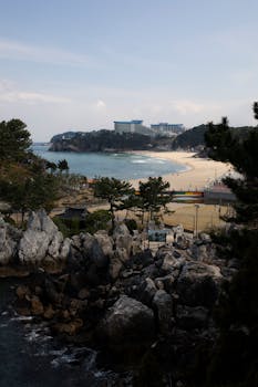 A tranquil beach scene featuring a rocky shoreline, sandy beach, and distant resort buildings.