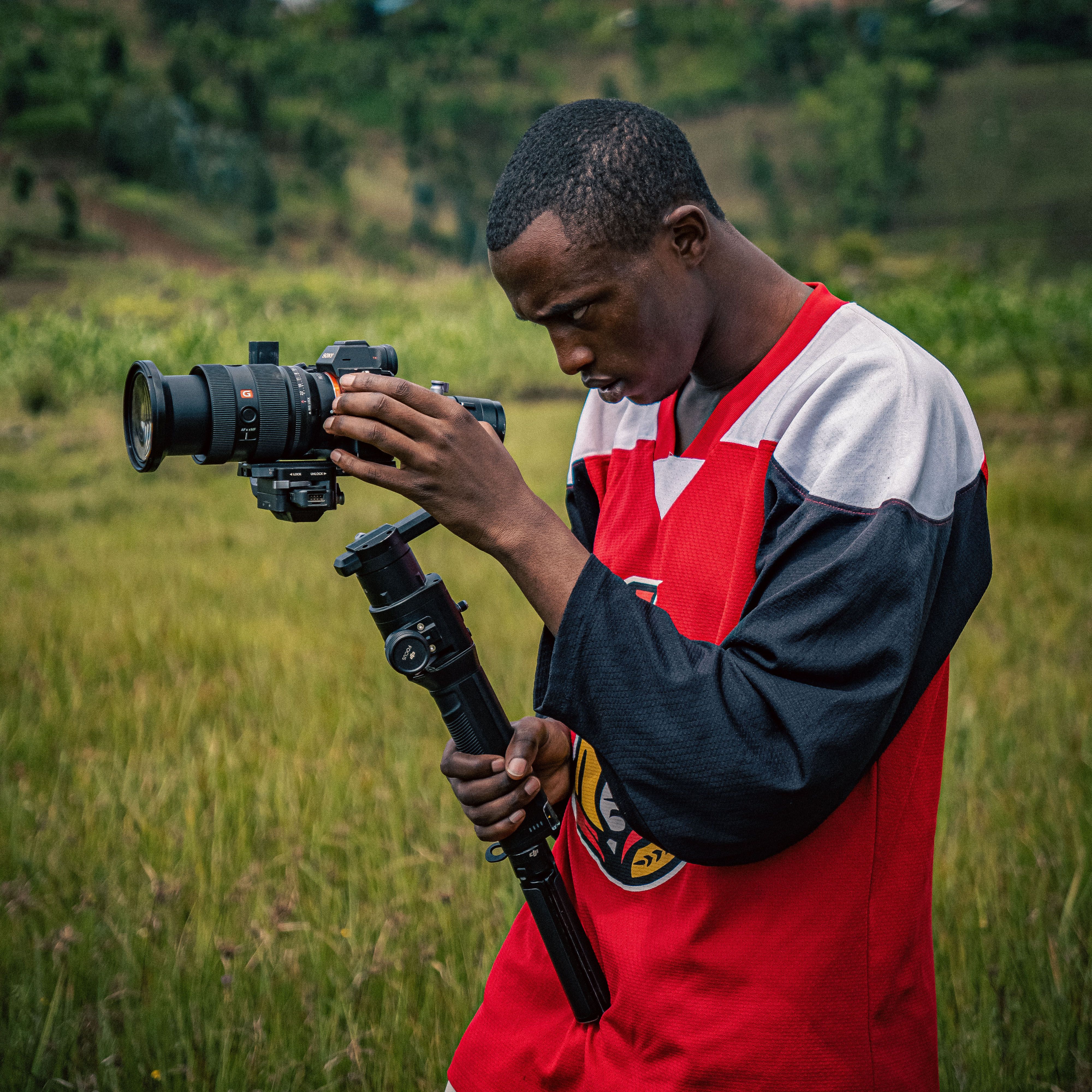 A focused photographer adjusting a camera outdoors in a lush green landscape, capturing the essence of nature and creativity.