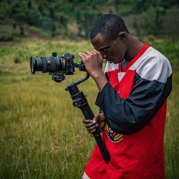 A focused videographer uses a gimbal outdoors to shoot scenic landscapes, showcasing dedication to craft.