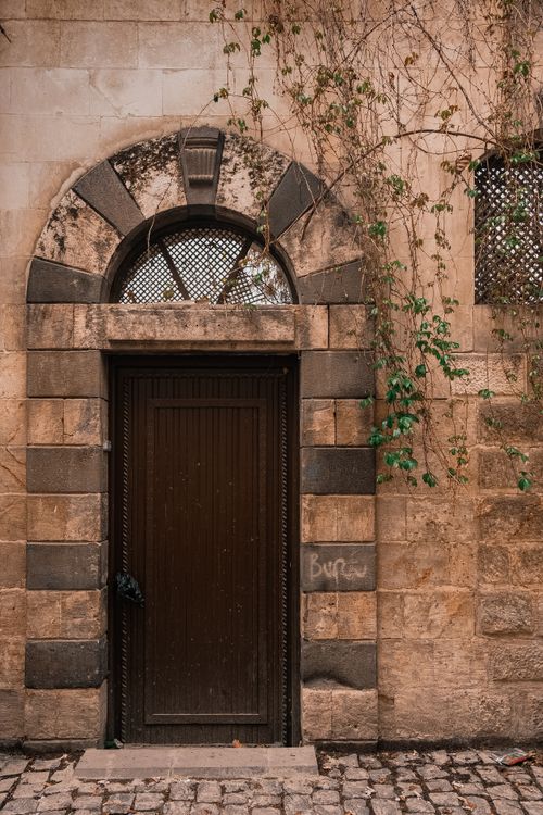 Free A classic arched wooden door set in a rustic stone building with climbing ivy. Stock Photo