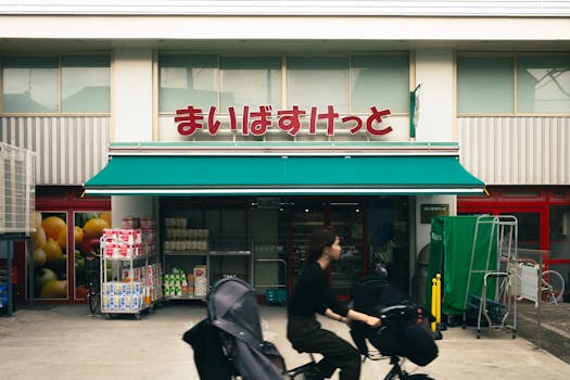 Woman rides bicycle past grocery store with Japanese signage in Tokyo.