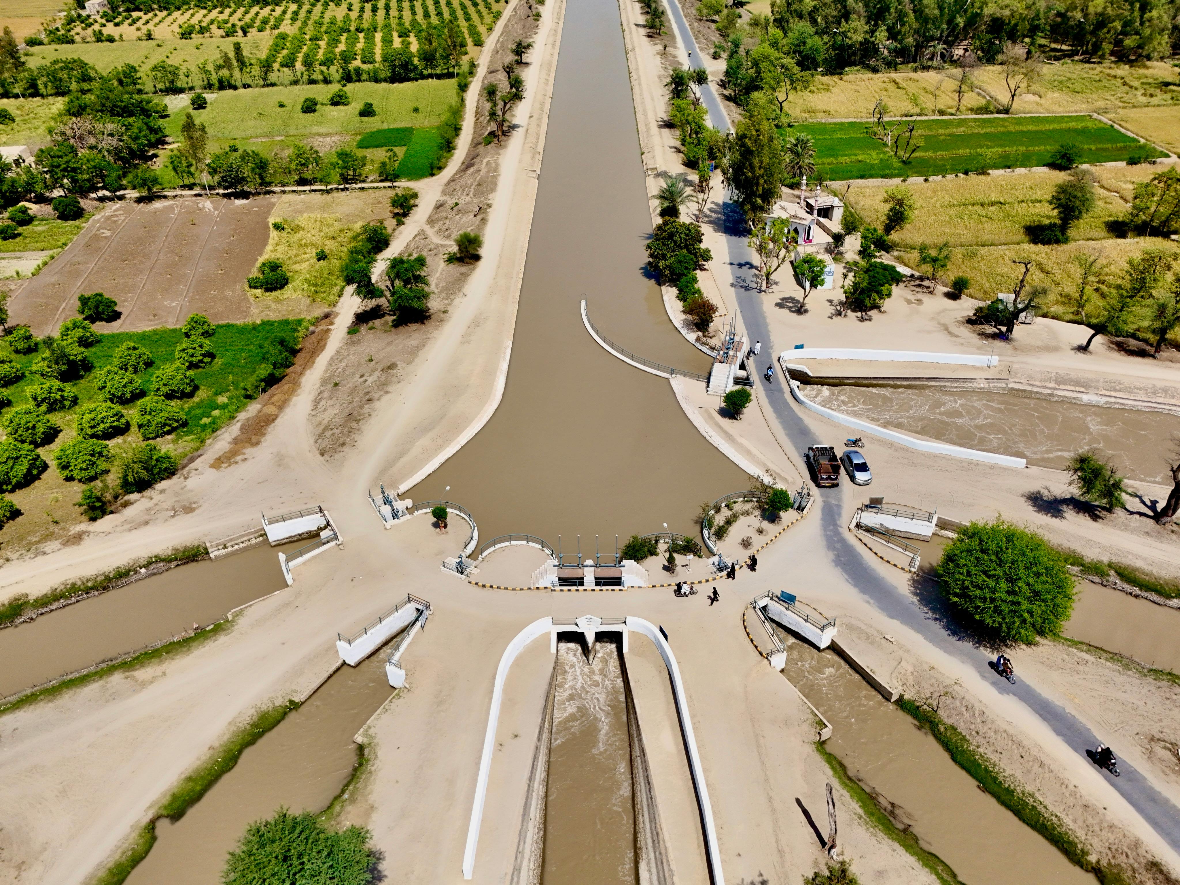 Aerial shot of irrigation canal surrounded by lush farmland, showing water distribution.
