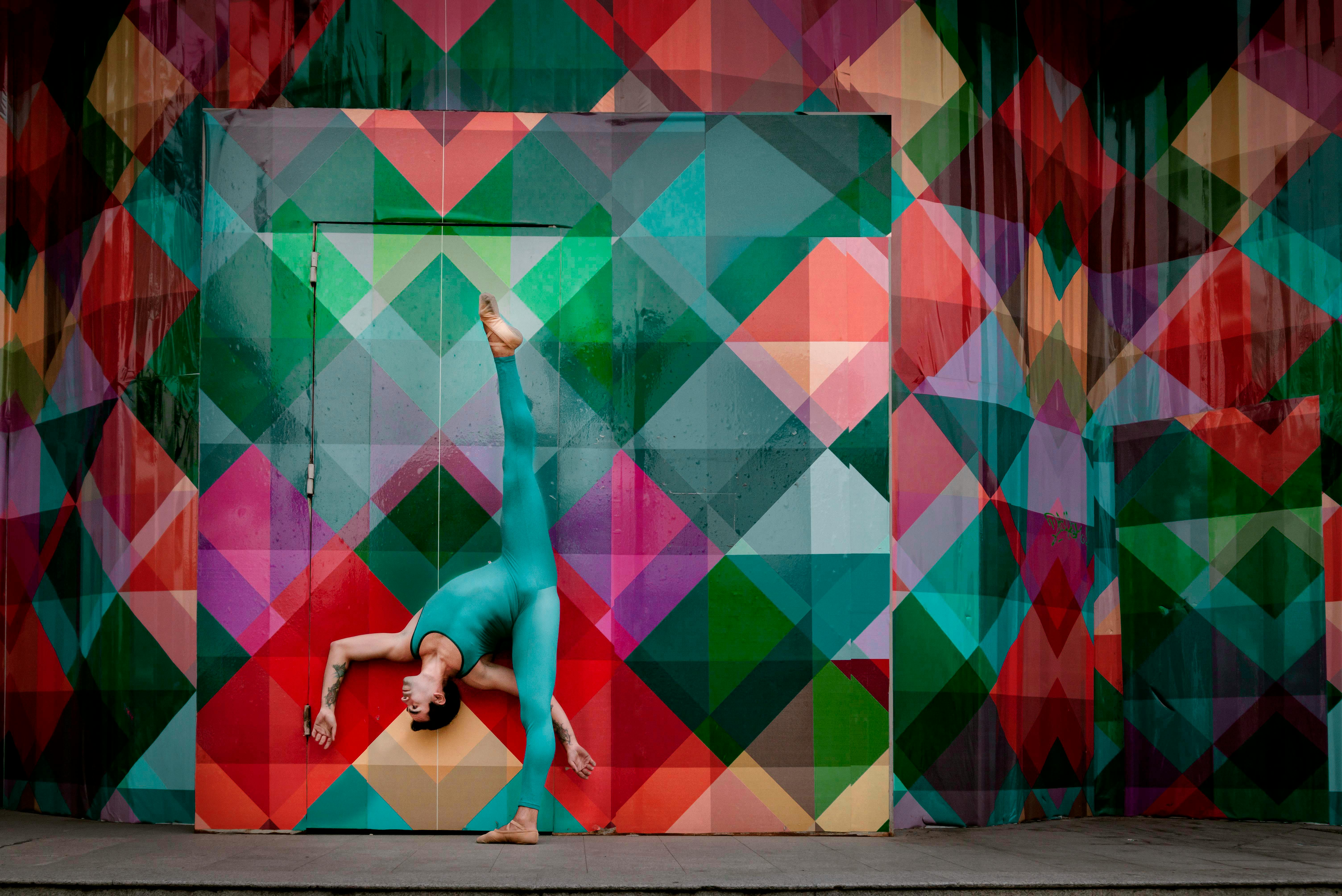 Free A vibrant acrobat performing a handstand against a colorful geometric patterned wall. Stock Photo