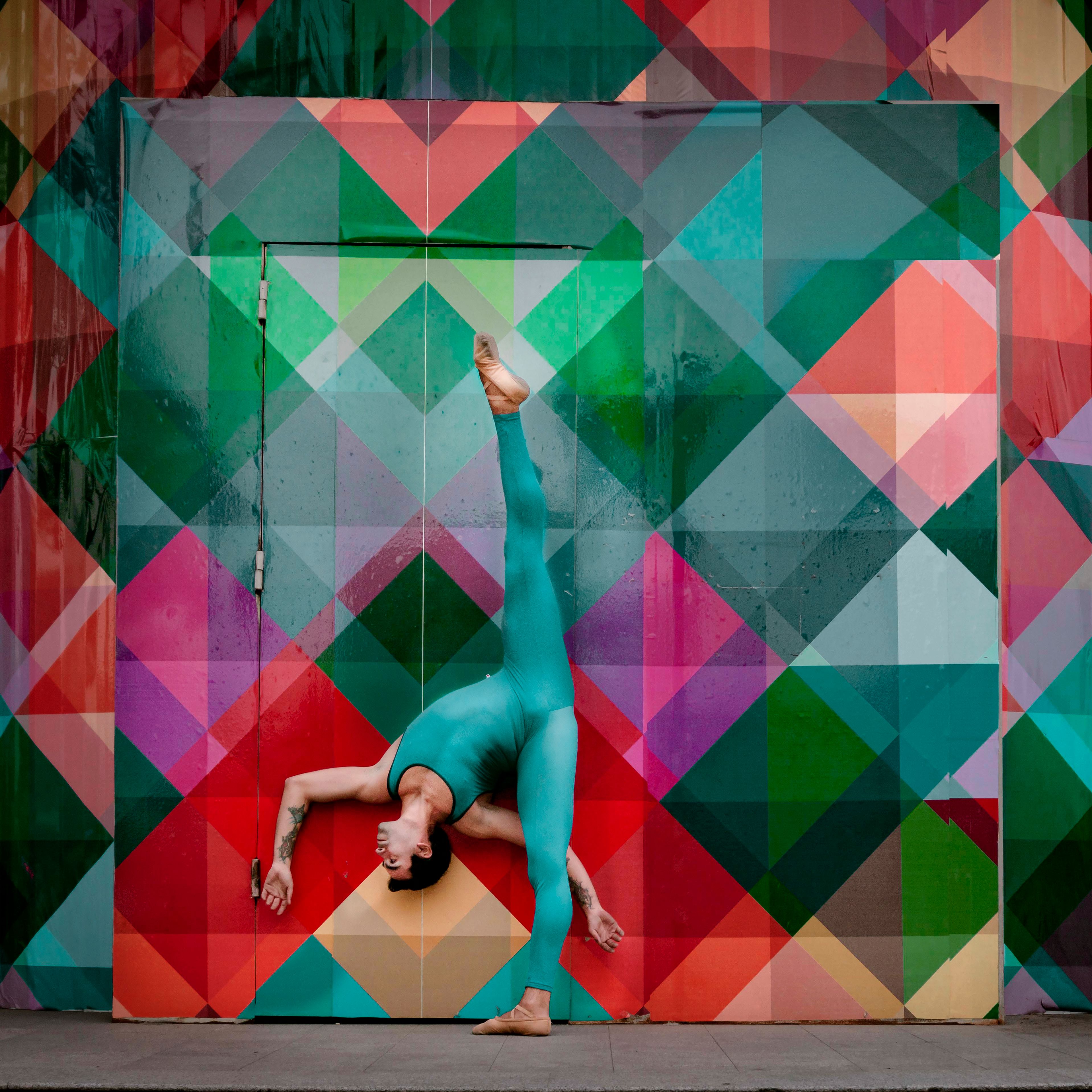 Graceful dancer in teal leotard performing under vibrant geometric mural.