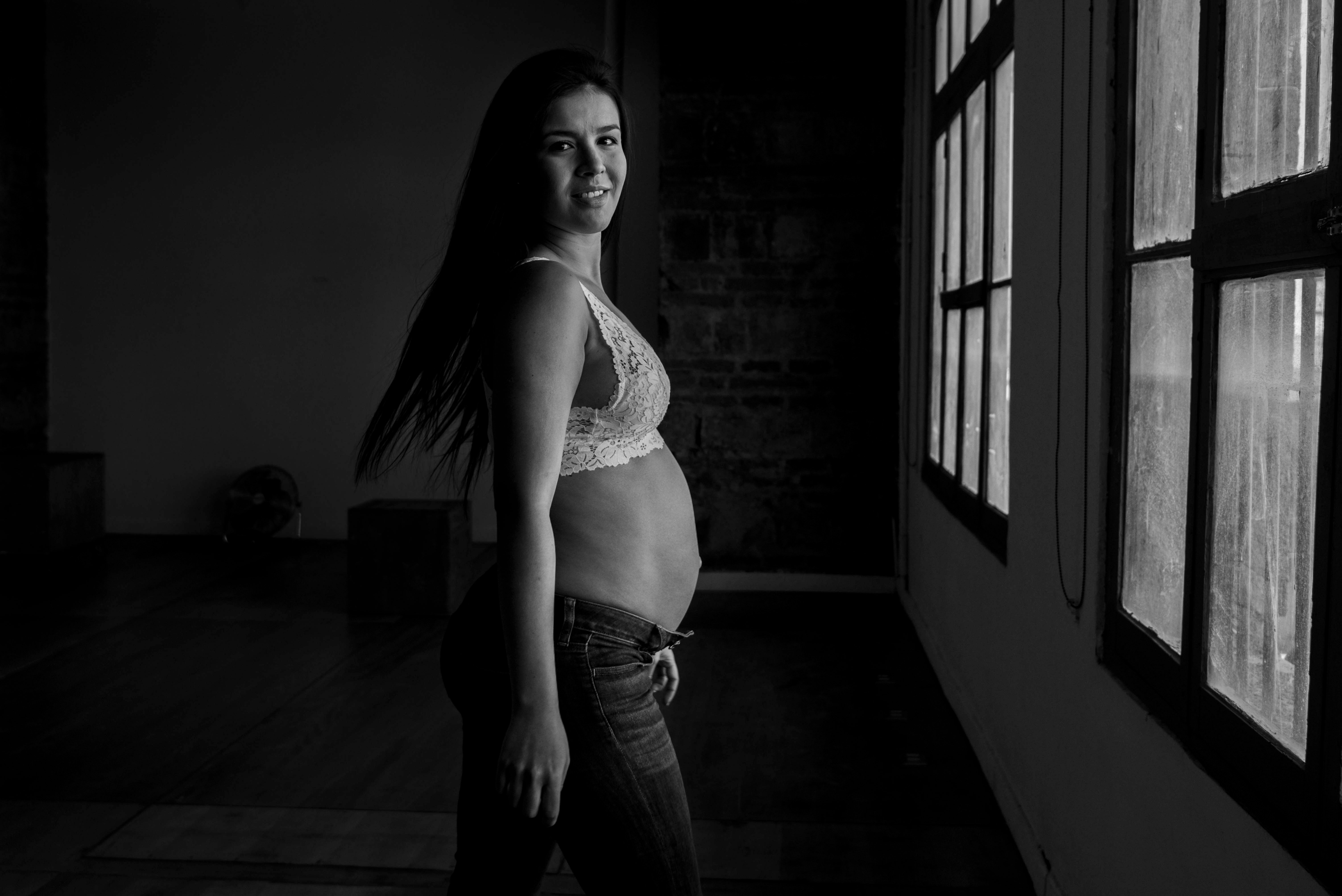 Artistic black and white portrait of a pregnant woman in a casual setting.