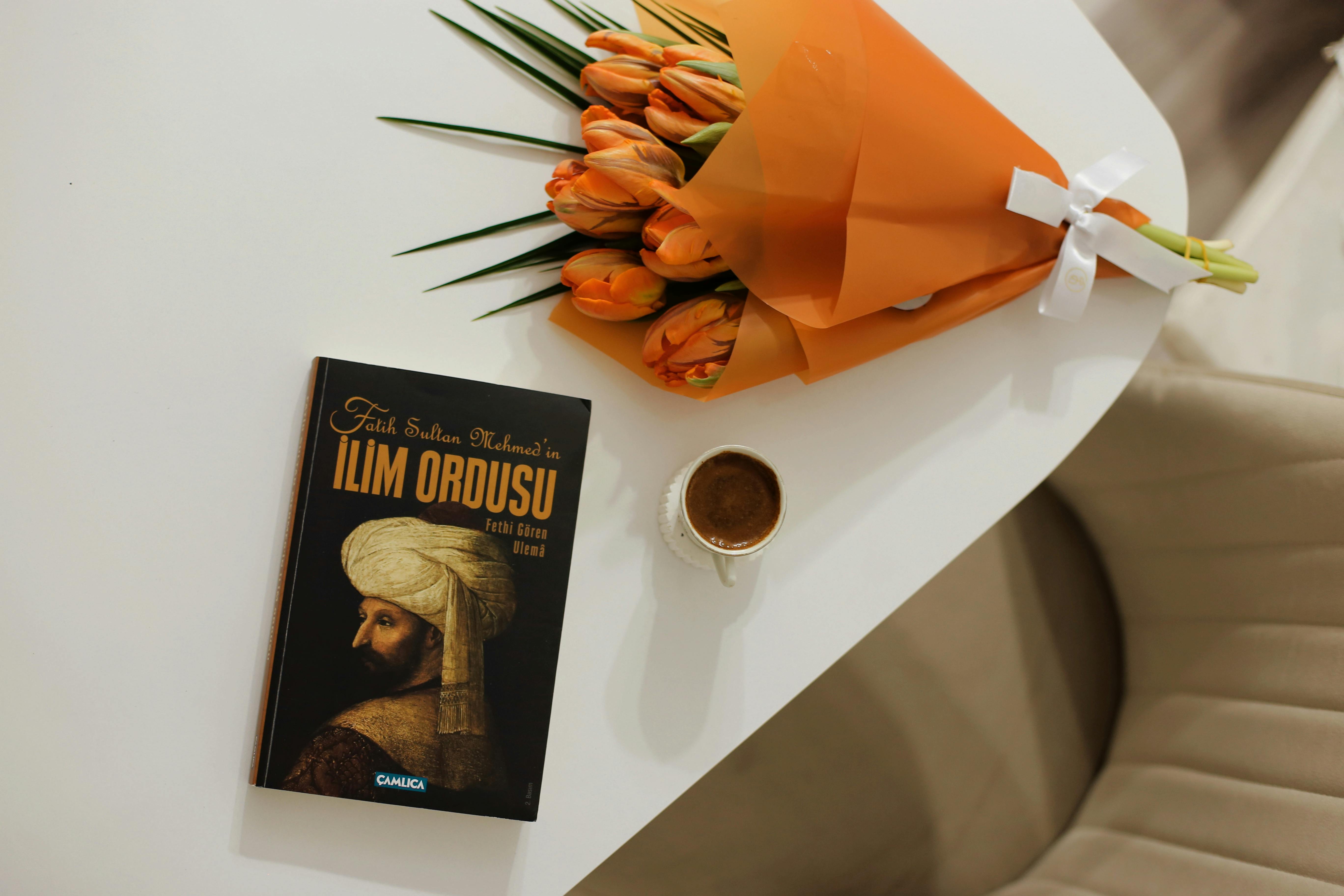 Orange tulips, coffee, and a historical book on a white table create a cozy scene.