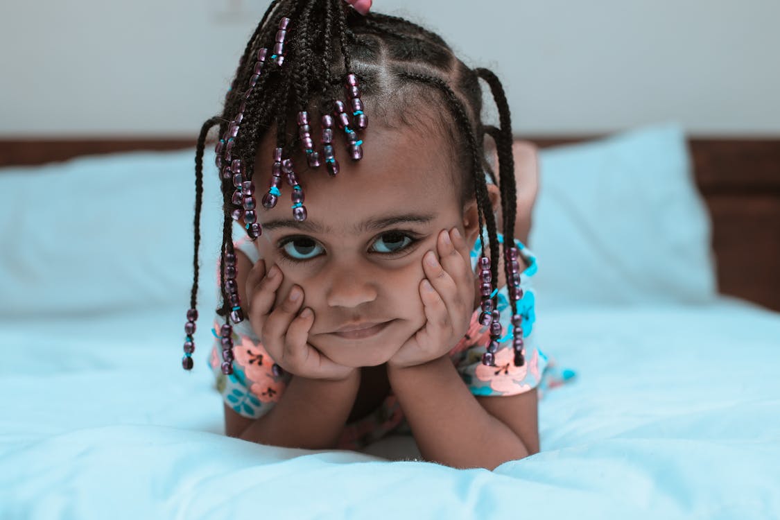 Selective Focus Photo of Little Girl Lying Forward on the Bed