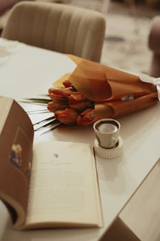 A warm indoor scene featuring a book, coffee cup, and a bouquet of tulips on a table.